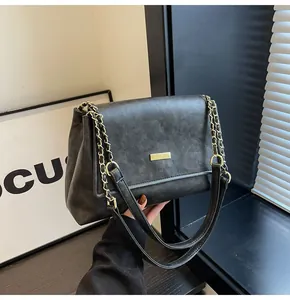 Detail of black textured leather crossbody bag with elegant gold chain and metal buckle