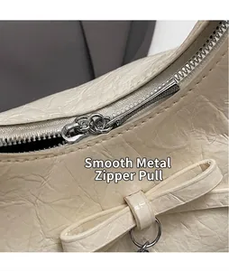 Macro-opname van de crèmekleurige tas met plooien, gladde metalen rits en een strikdetail