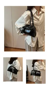 Detail of black glossy shoulder bag with white pearl bow accent and zipper closure