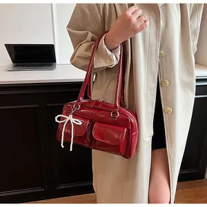 Detail of red patent leather Boston bag with side pockets and pearl bow charm