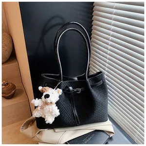 Close-up of black woven tote bag with leather straps and a white plush bear charm