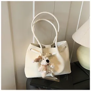 Close-up of cream woven tote bag with leather handles and a cute plush bear charm