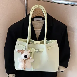 Pale green woven tote bag with a plush bear charm hanging on a dark suit blazer