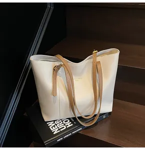Detail view of cream white tote bag with brown straps placed on books by a staircase
