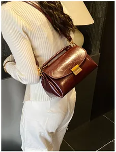 Sac bandoulière en cuir verni rouge foncé porté par un mannequin dans un salon