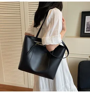 Detailed view of black matte leather tote bag worn by model over a white dress