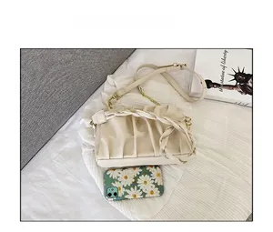 Detail view of cream pleated cloud bag with gold chain and woven handle next to phone