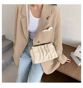 Beige pleated cloud crossbody bag with gold chain strap shown in a lifestyle setting