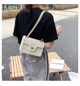 Detail of straw woven crossbody bag with pearl trim and gold chain strap outdoors