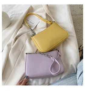Detalle de bolsos baguette amarillos y morados con cadenas de plata sobre tela blanca