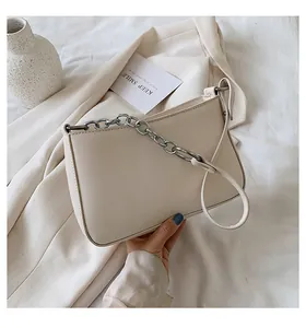 Vista superior de un bolso baguette de cuero crema con cadena plateada sobre blazer beige