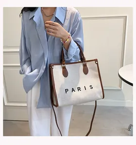Detail of a beige canvas tote bag with brown leather trim and Paris logo print