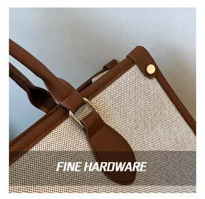 Macro detail of golden metal D-ring and reinforced brown leather trim on canvas tote bag