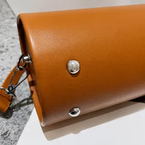 Detailed macro view of the brown leather cylinder bag base with silver metal protective studs