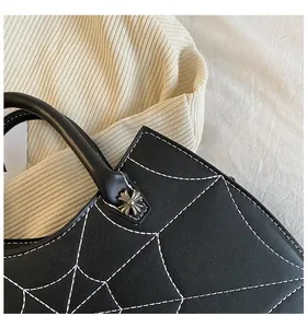Close-up of black PU leather bag featuring white spider web stitching and metal cross rivets