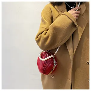 Dettaglio borsa a conchiglia rossa trasparente con tracolla di perle su cappotto