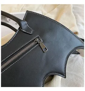 Close-up of gothic bat-shaped black PU leather bag with white contrast stitching and zipper