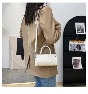 Minimalist white cylindrical handbag with curved top handle and shoulder strap worn by model