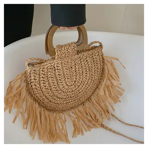 Detail of bohemian straw bag with fringe decoration and smooth wooden handle