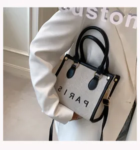 Detail view of canvas tote bag with PARIS lettering and gold-tone hardware on ivory suit