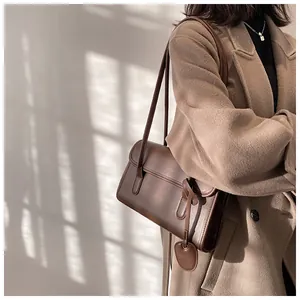 Detail of dark brown leather shoulder bag with heart tag on a camel wool coat