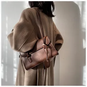 Detail shot of a vintage brown leather underarm bag featuring a knot strap on a wool coat