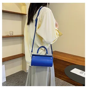 Blue cylindrical PU leather crossbody bag worn by a model in a minimalist home setting