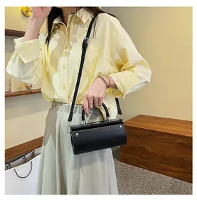 Close-up of black barrel handbag with silver hardware held by a fashionably dressed model