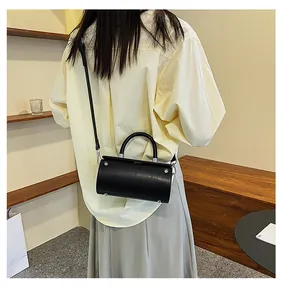 Back view of a woman wearing the black leather cylindrical bag with silver hardware