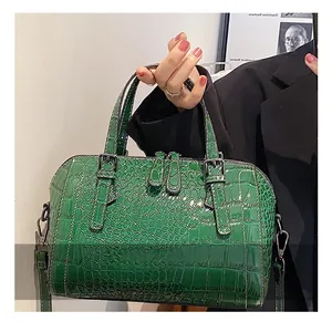 Detail of green crocodile texture handbag featuring adjustable buckle handles and glossy finish