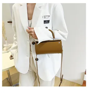 Brown cylinder shoulder bag worn with a white blazer in a modern minimalist indoor setting