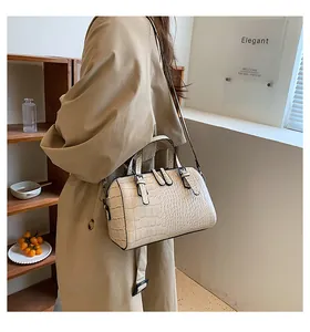 Detail of beige crocodile pattern bag shown on model with dual handles and long strap