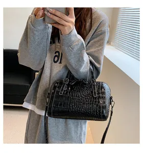 Close-up of black crocodile pattern Boston bag with white stitching and leather handles