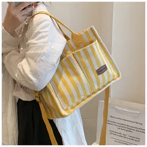 Side view of yellow and white striped canvas tote bag with brown leather label and straps