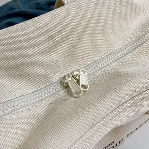 Detail van de soepele plastic dubbele ritsen op beige stevige canvas draagtas