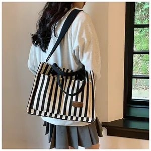Detail of striped canvas tote bag showing wide fabric strap and brown leather label