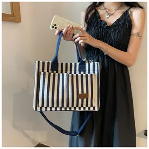 Detail of blue and white striped canvas tote bag with front pockets and leather label