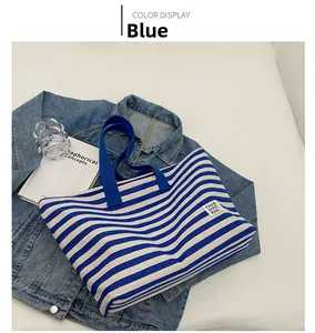 Detail view of large striped canvas tote bag with blue handles and fashion label