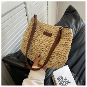 Detail of woven straw shoulder bag with dark brown leather straps held against lifestyle background