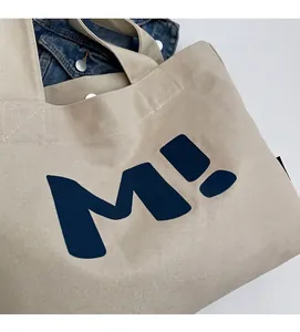 Detail of cross-stitch reinforcement and blue letter print on beige canvas tote bag