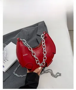 Dettaglio borsa a mezzaluna rossa in pelle con catena d'oro e logo CGER. su sfondo neutro