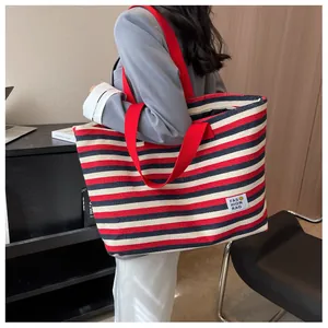Detail of large canvas tote bag featuring red and blue stripes with fashion logo patch