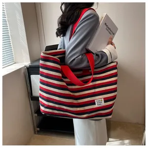 Detail of a large striped canvas tote bag with red strap and decorative logo patch