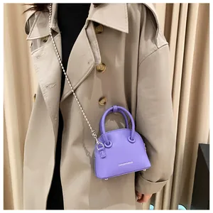 Detail of purple crossbody bag with silver bead chain shown on a beige trench coat