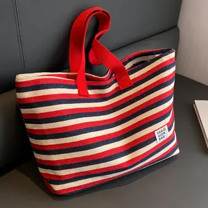 Large striped canvas tote bag with red handles and fashion patch on a grey background