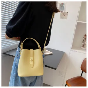 Detail of a light yellow leather bucket bag featuring a gold metal twist lock and shoulder strap