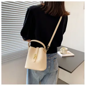 Minimalist beige bucket bag with gold clasp shown on a model for scale and style