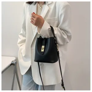 Model wearing a black PU bucket bag with gold hardware and adjustable shoulder strap