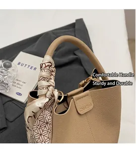 Dettaglio della borsa a secchiello beige in pelle con manico decorato da sciarpa in seta