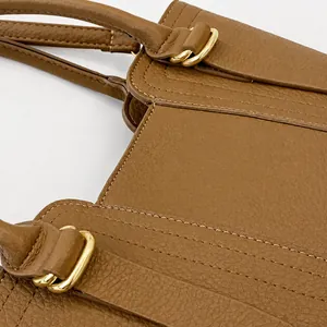 Detail of brown litchi leather handbag with gold metal buckle and precision stitching